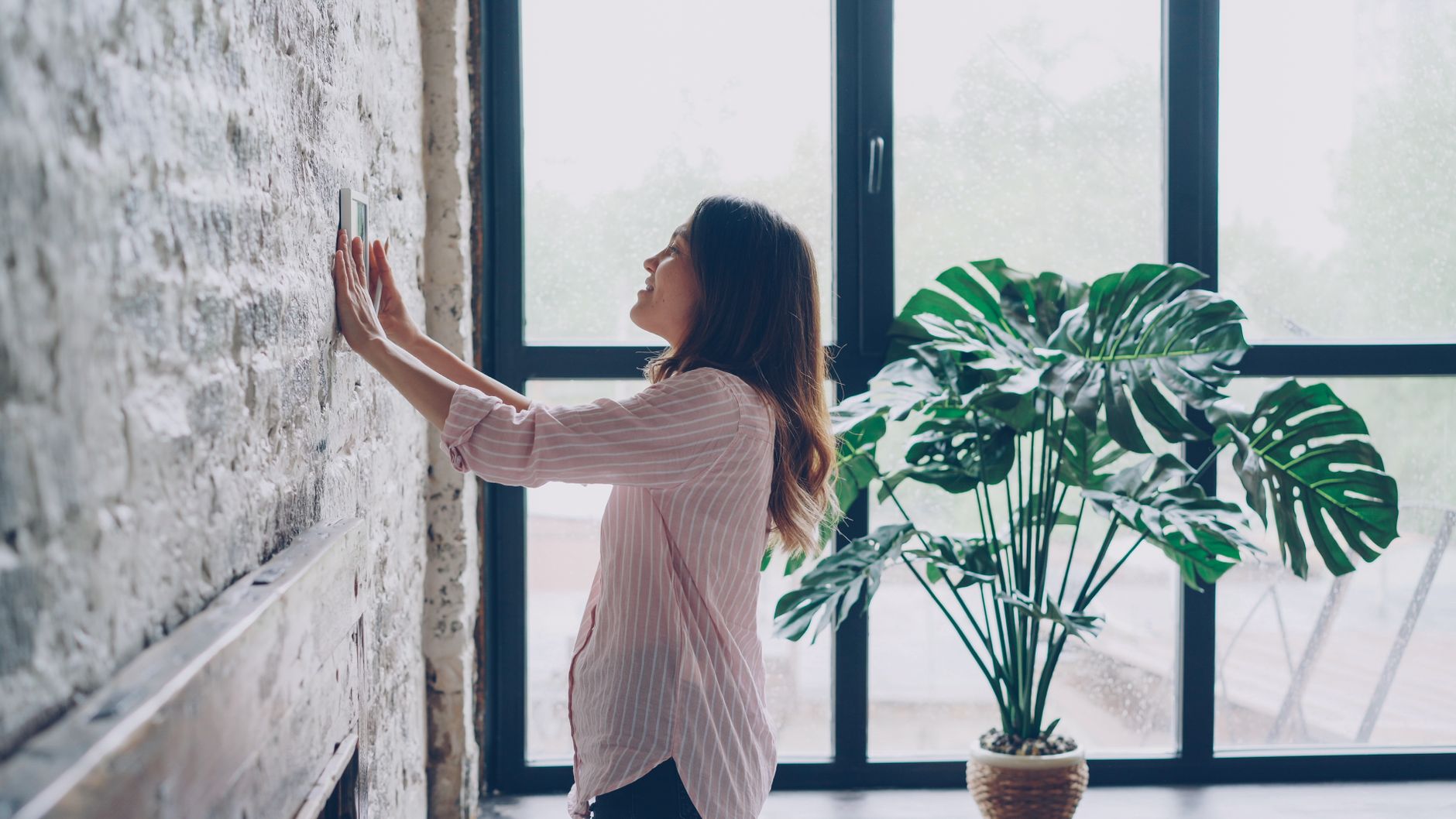 Femme ajustant le thermostat près d’une grande fenêtre